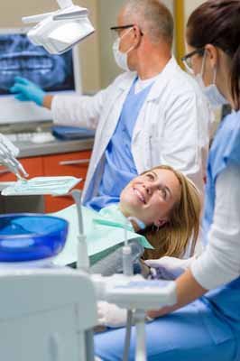 Photo of a woman in a dental chair with a dentist and hygienst on either side of her; for information on affordable dentistry from Plano TX female dentist Dr. Miranda Lacy.