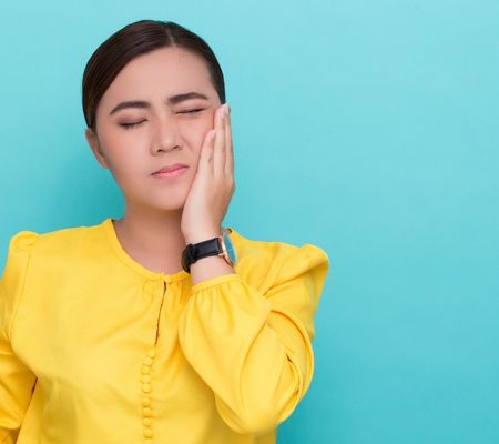 Young Asian woman holding the side of her face portraying root canal tooth issues